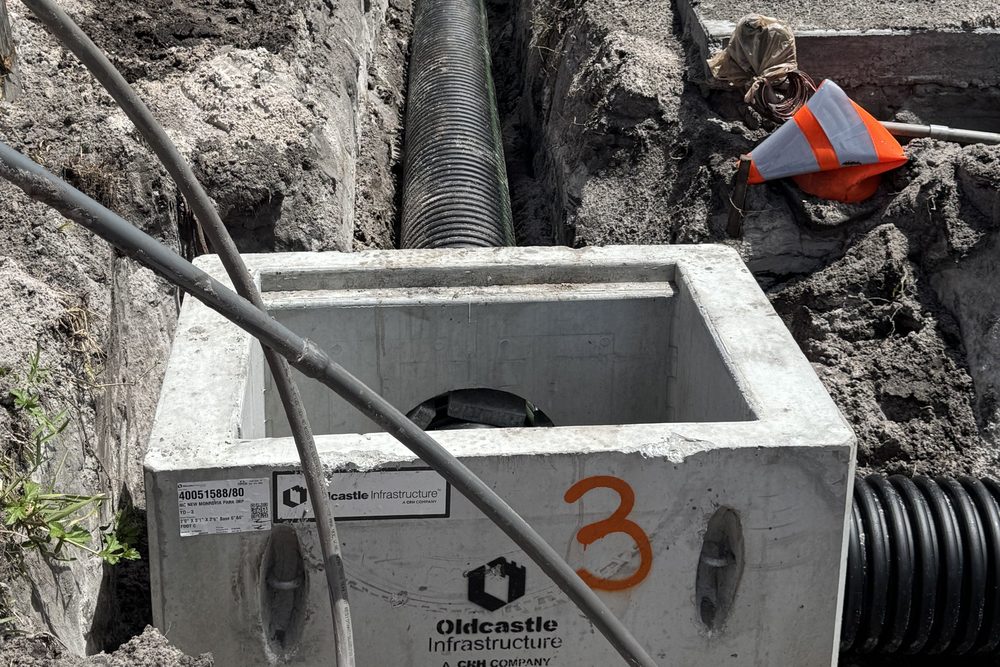 Crew installing a precast concrete storm box and drainage pipe